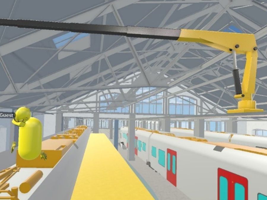 Virtual representation of a train maintenance hall with roof structure, trains on parallel tracks and a yellow crane arm positioned above the vehicle for maintenance work.