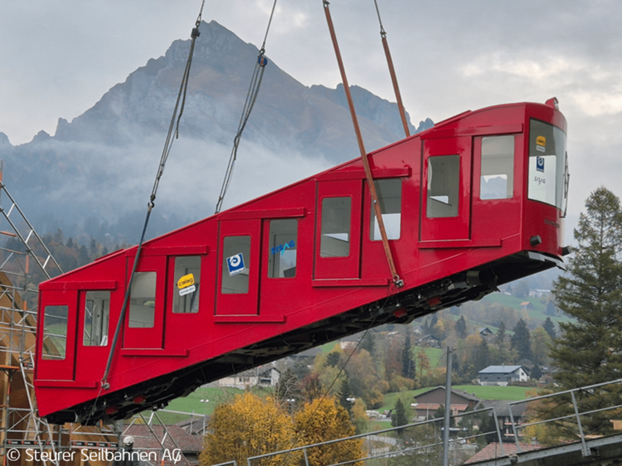 Assembly of a red funicular carriage with new air suspension chassis during the modernisation of an alpine funicular railway, accompanied by PROSE.