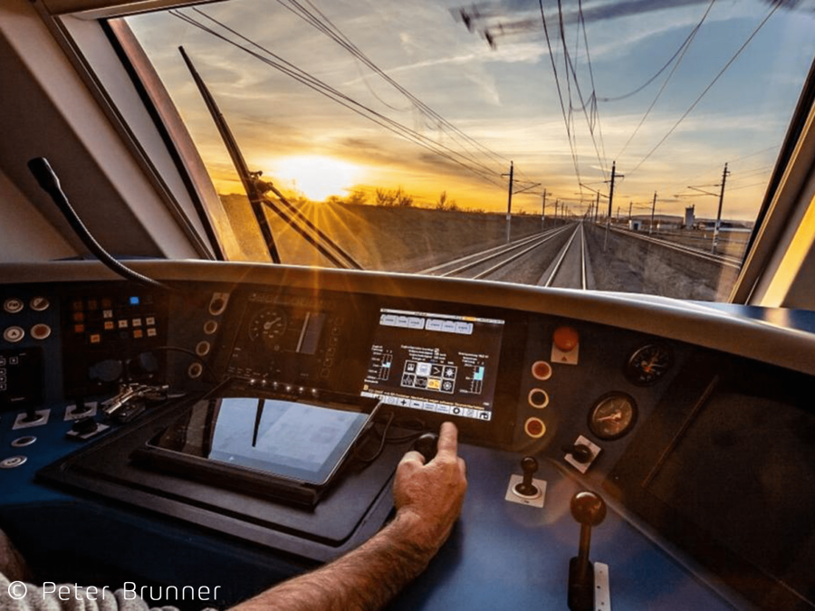 Lokführer in einem modernen Hochgeschwindigkeitszug mit digitalen Steuerungen, symbolisiert fortschrittliche Bahnsysteme und Zertifizierungsprozesse.