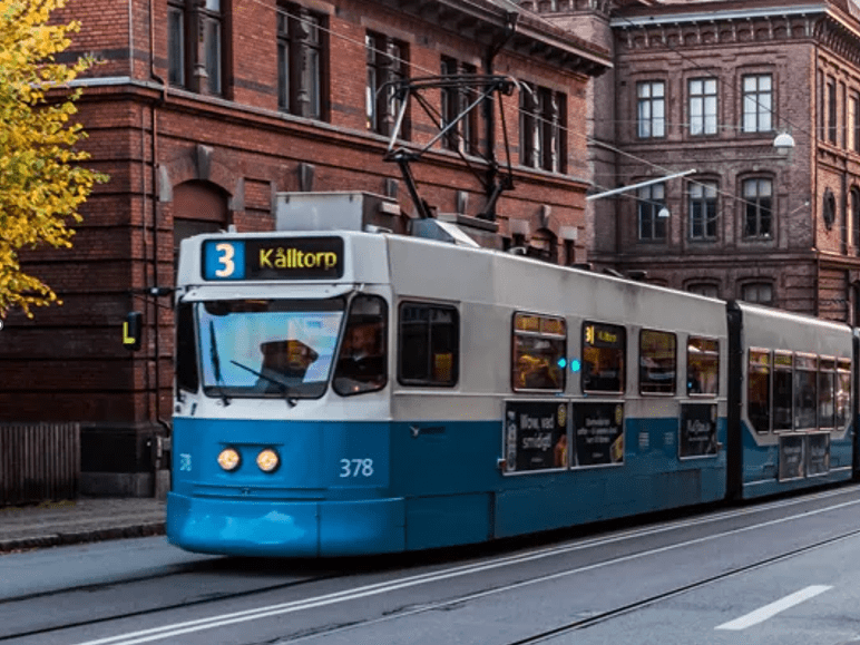 Blue and white Västtrafik tram on route 3 to Kålltorp travelling through a historic city street in Gothenburg, Sweden.